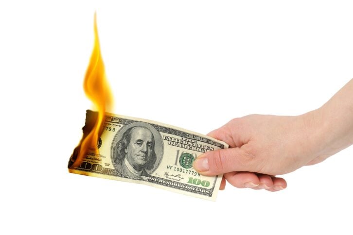 burning $100 dollar bill in hand
