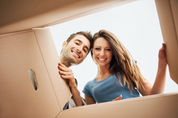 smiling young couple opening a carton box and looking inside