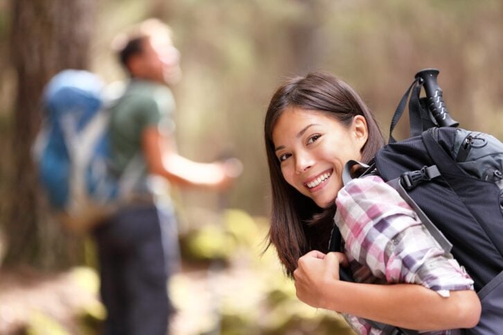 woman hiker smiling in forest with male hiker in the background