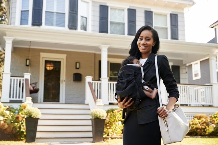 Mom standing outside of her home ready to go to work with baby on her chest