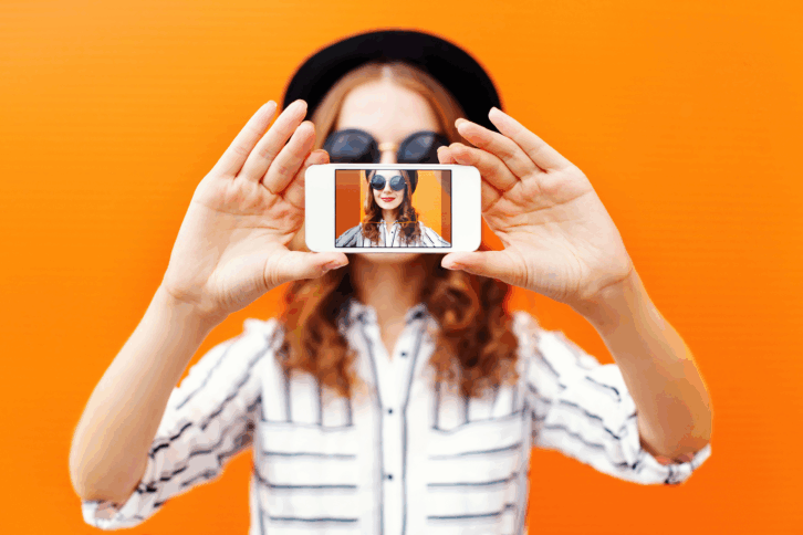 Woman taking a selfie with an orange backdrop