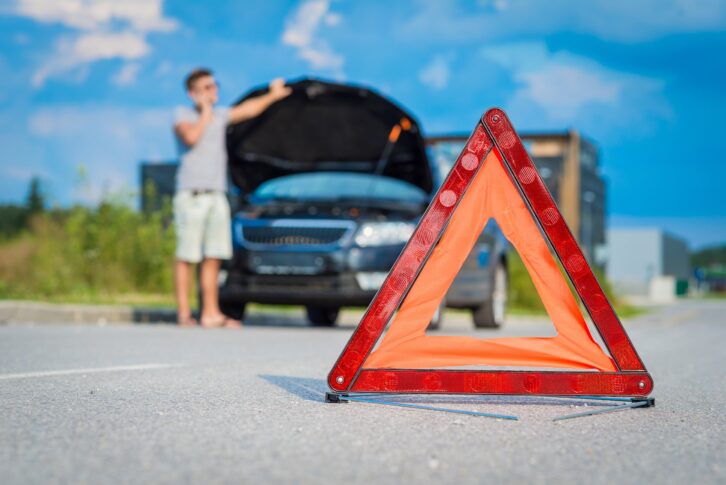 red warning triangle on road with broken car and person on cell in background