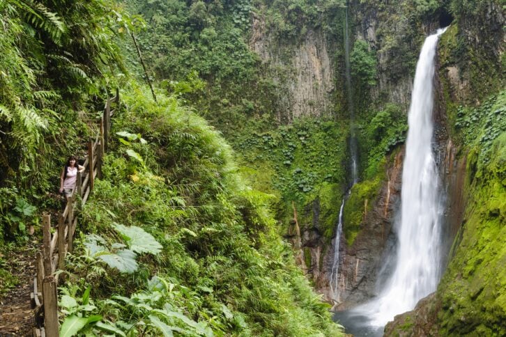 woman standing in front of towering tropical waterfall in Costa Rica