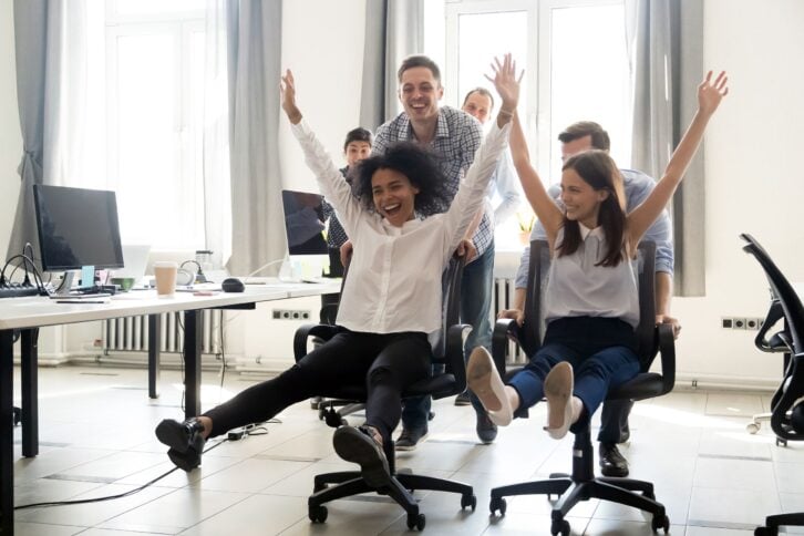 diverse excited workers having fun riding on chairs on Friday
