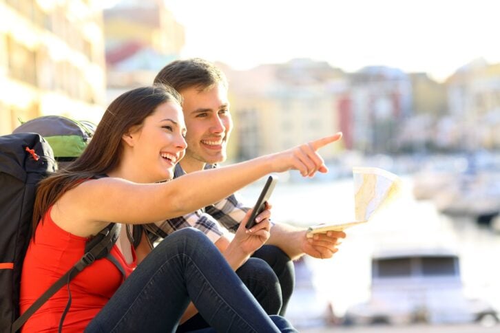 two happy tourists searching location together with a phone and map and pointing with the finger