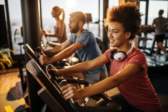 happy black athlete practicing on exercise bike in a health club