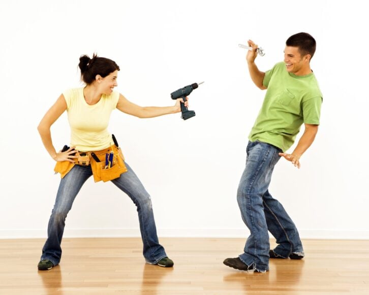 woman pointing drill playfully at man smiling and laughing in home