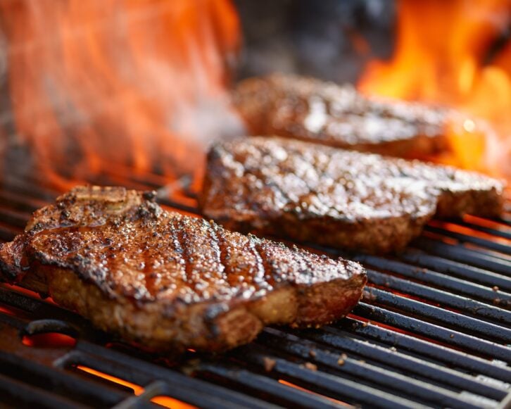 grilling steaks on flaming grill