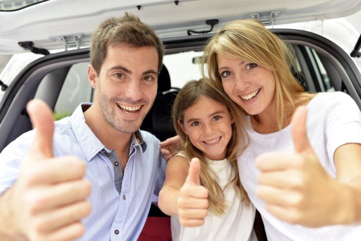cheerful family showing thumbs up while sitting at the back of a SUV