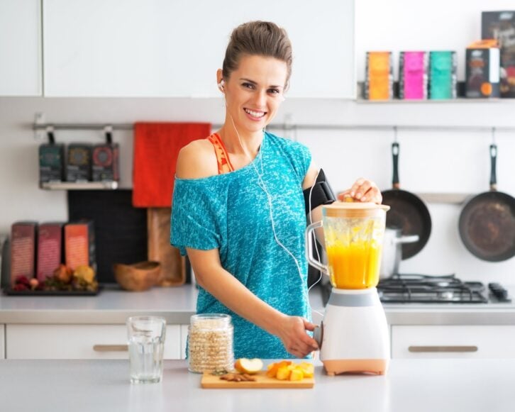 happy fitness young woman making pumpkin smoothie in kitchen