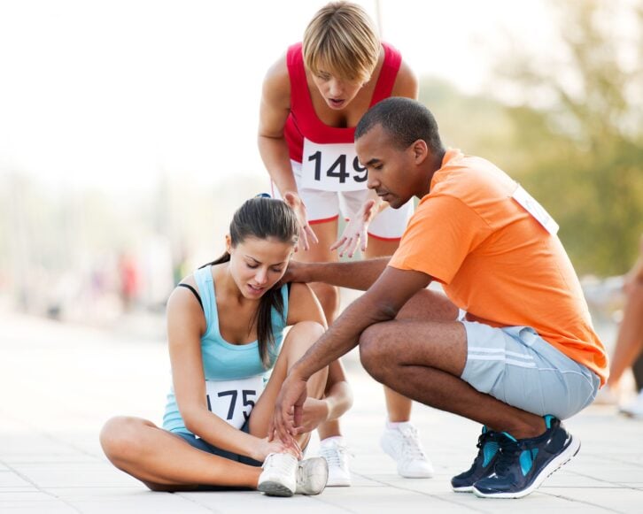 young woman at the competition with sprained ankle, two people helping her