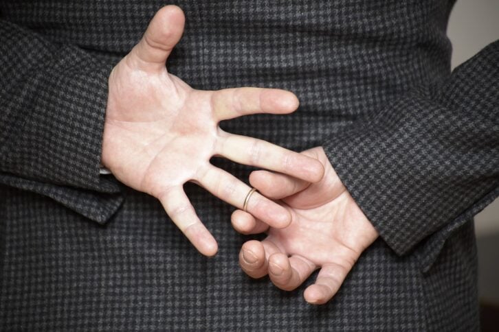 man in struggling to remove wedding ring from his finger holding hands behind his back