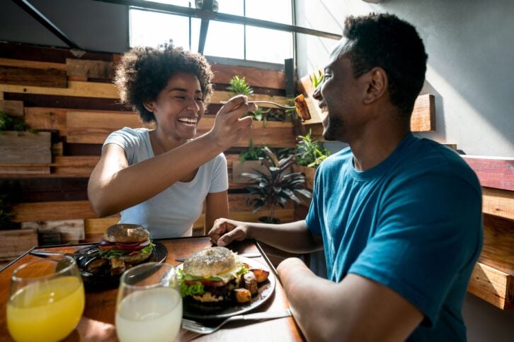 happy African American couple at a restaurant and woman feeding her boyfriend