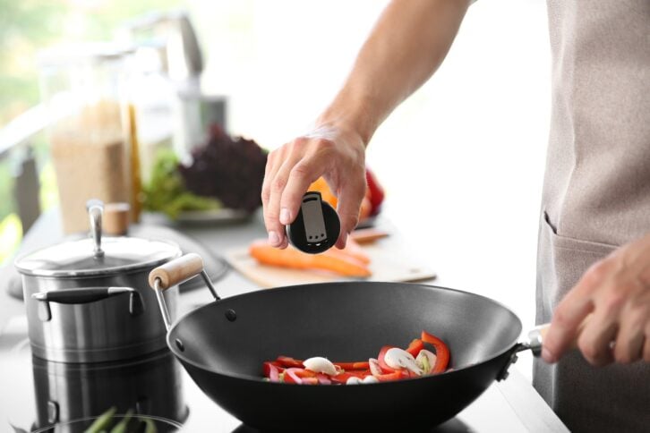 male hand adding salt to vegetables in pan