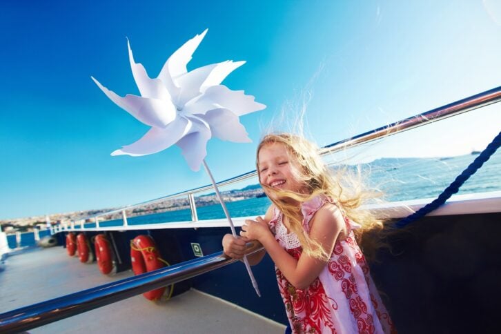 cute blonde small girl playing with pinwheel on cruise ship deck