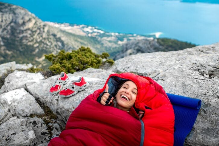 Young woman lying in red sleeping bag on a rocky mountain