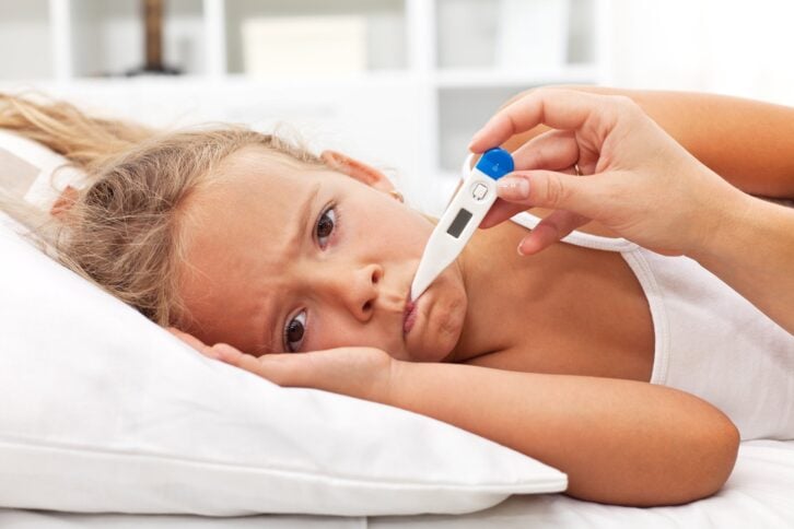 sick little girl holding thermometer laying in bed with grumpy face