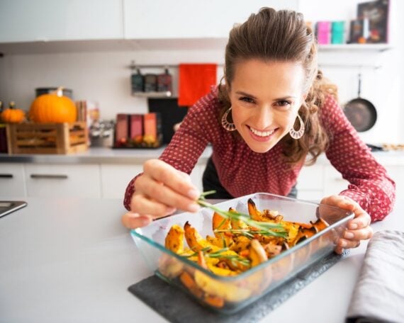 woman in kitchen putting rosemary on squash dish