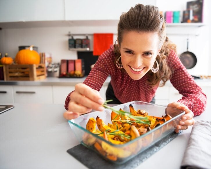woman in kitchen putting rosemary on squash dish