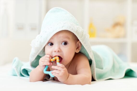 Baby with teething toy in mouth and towel on head