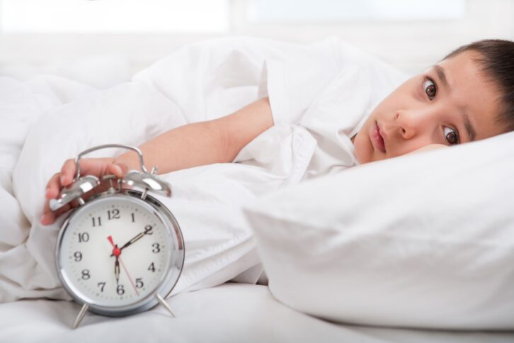 sleepless little boy laying in bed with clock