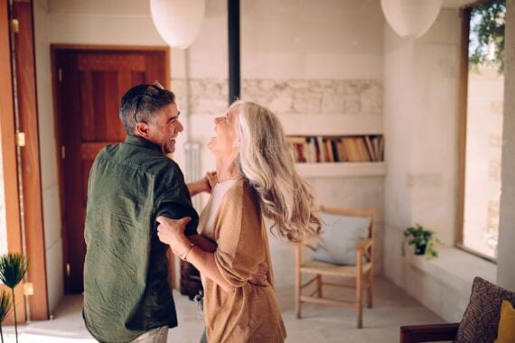 happy senior couple dancing and laughing together at home