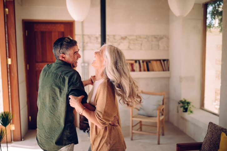 happy senior couple dancing and laughing together at home
