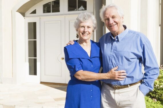 senior couple standing outside house