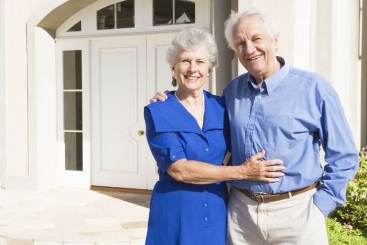 senior couple standing outside house