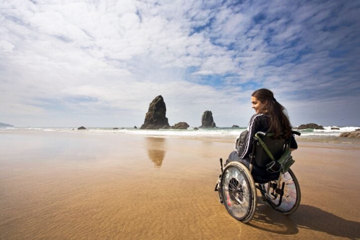 young woman in wheelchair on beach in pacific coast of united states