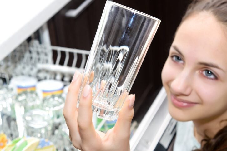 woman looking at clean glass while unloading dishwasher