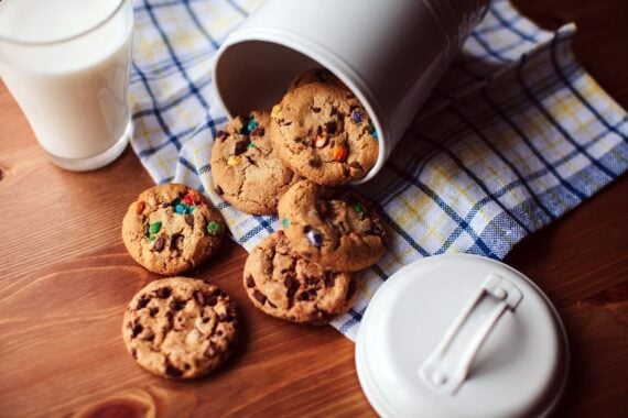 Assorted cookies falling out of a jar on a wooden table with a glass of milk