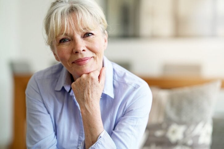 Senior woman sitting on couch at home looking pensive at the camera