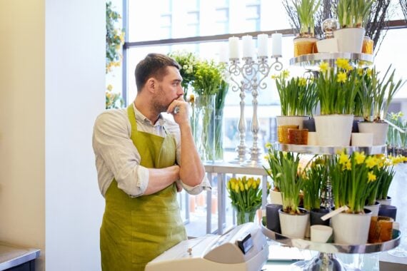sad florist man with cashbox standing at flower shop counter