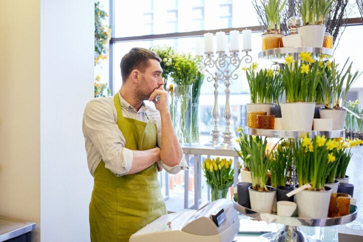 sad florist man with cashbox standing at flower shop counter