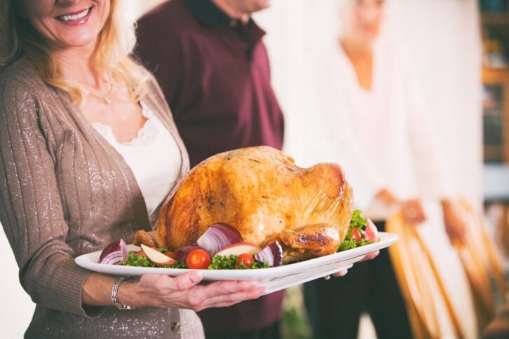 Woman holding platter with roasted turkey for Thanksgiving
