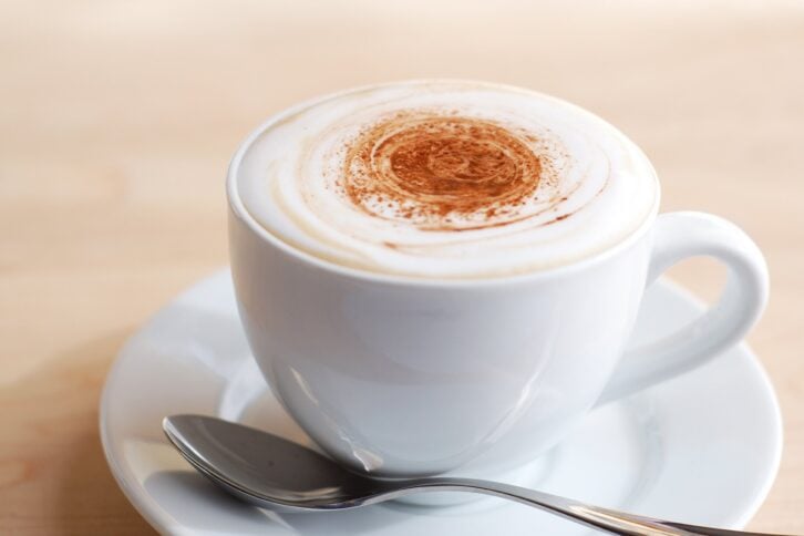creamy cappuccino in white cup on wooden surface