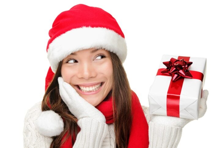 Happy young woman holding a present and looking sideways wearing a Santa hat