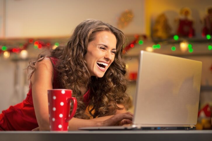 happy housewife with cup of hot chocolate using laptop in christmas decorated kitchen