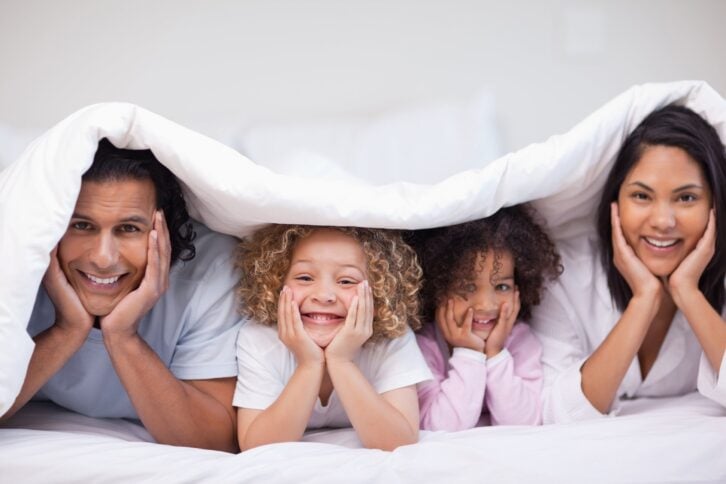 family hiding under the covers in bed