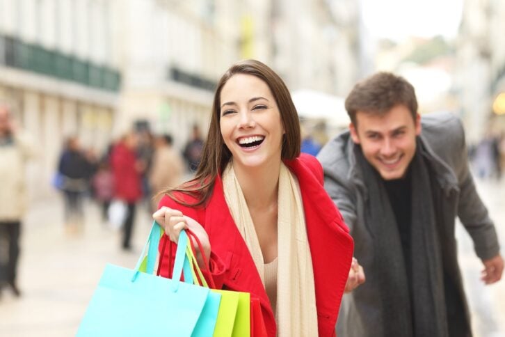 casual couple of shoppers running in the street towards camera holding colorful shopping bags