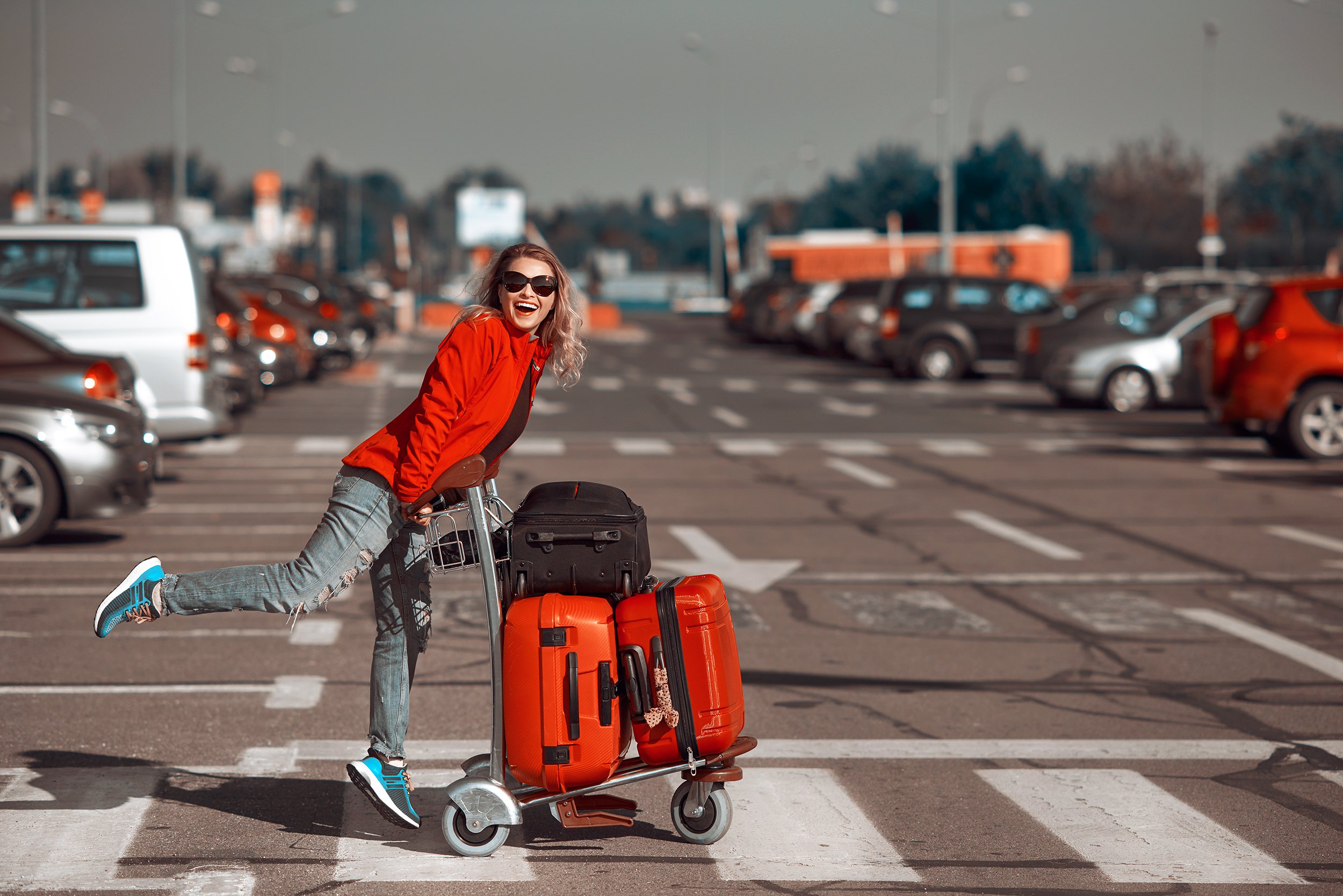 happy woman with bags on cart in airport parking lot