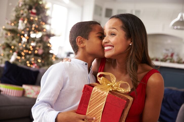 Happy mom receiving a gift and a kiss on her cheek from her young son on Christmas
