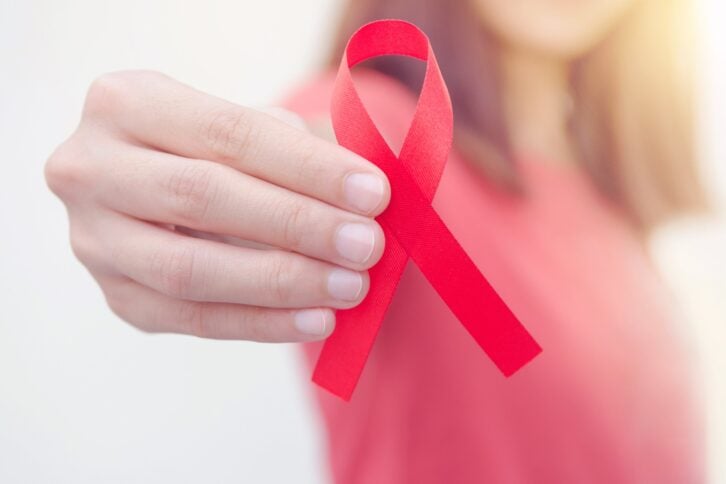 woman's hand holding red HIV, AIDS awareness ribbon