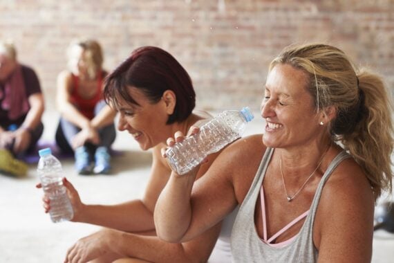 two women laughing and drinking from water bottles in the gym