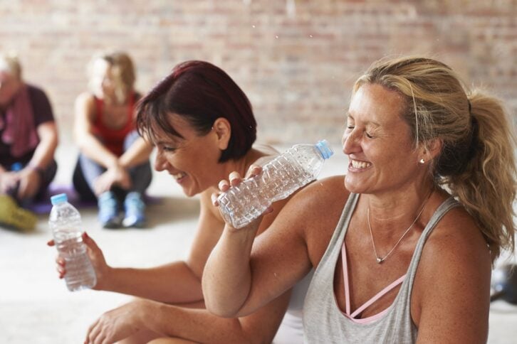 two women laughing and drinking from water bottles in the gym
