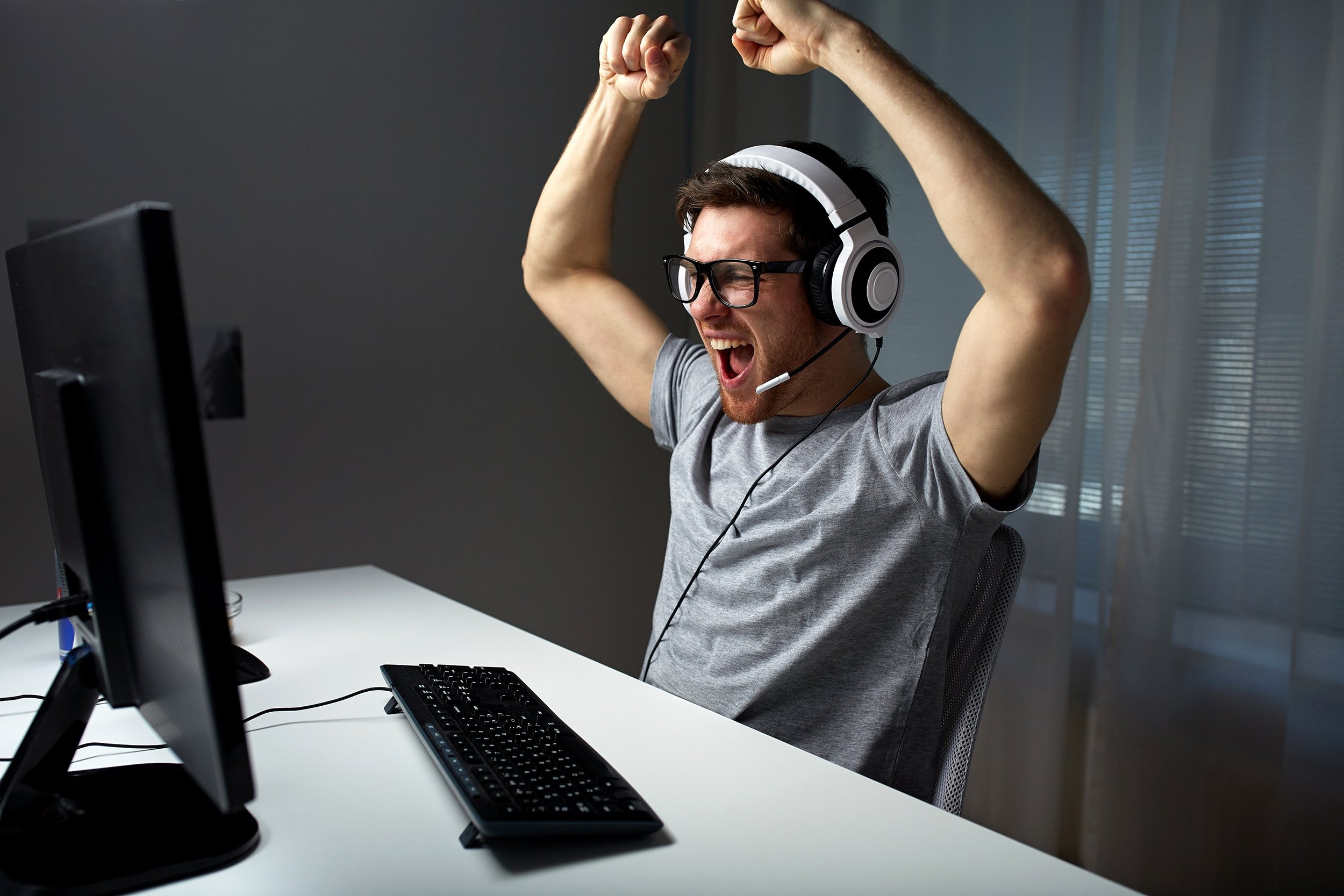 young man in eyeglasses with headset playing and winning computer game at home