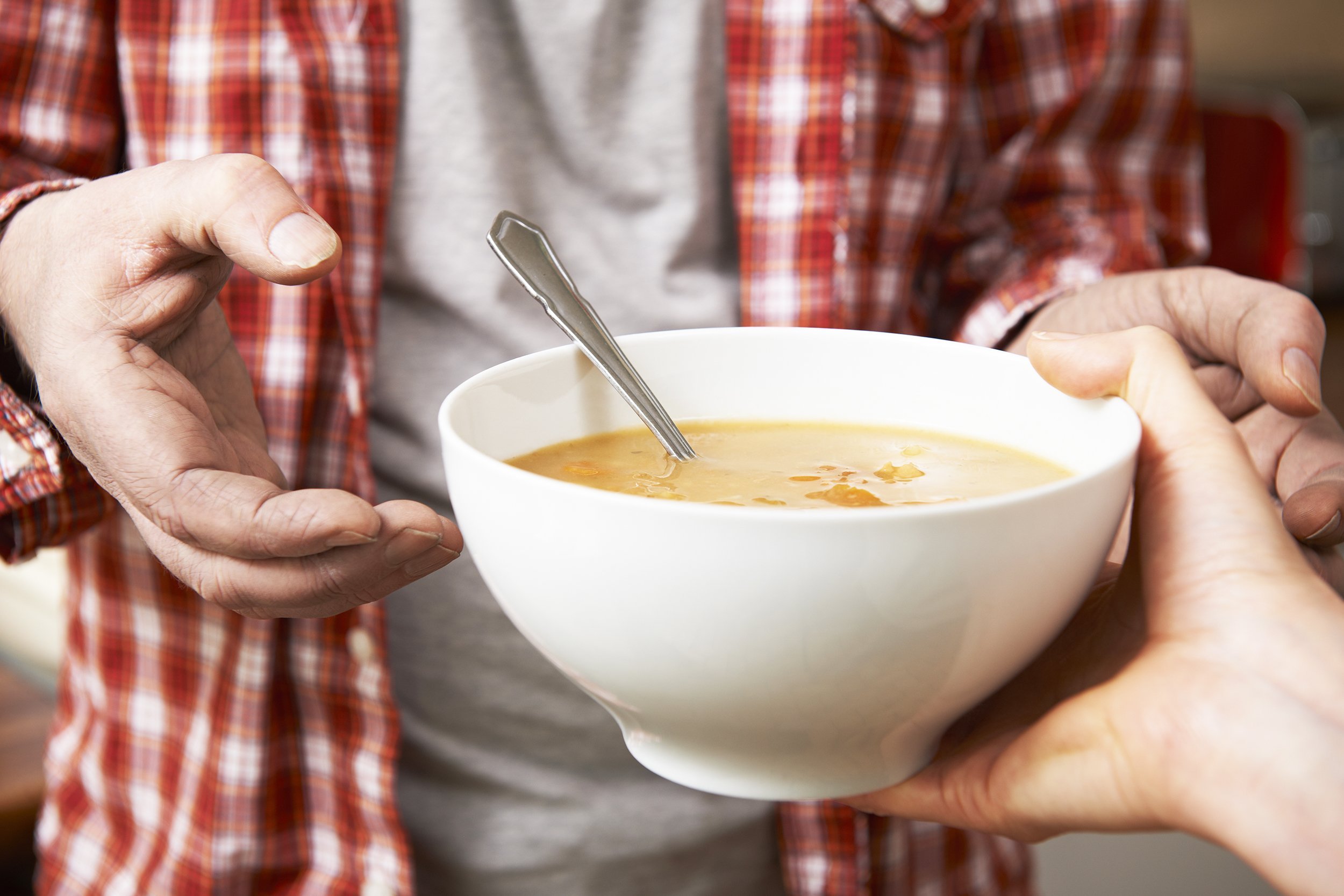 homeless man being handed bowl of soup by volunteer