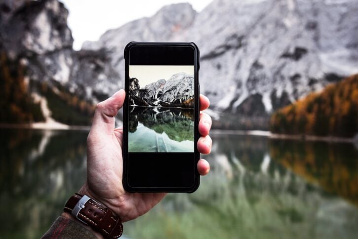 Closeup of smart phone taking picture of mountains and lake