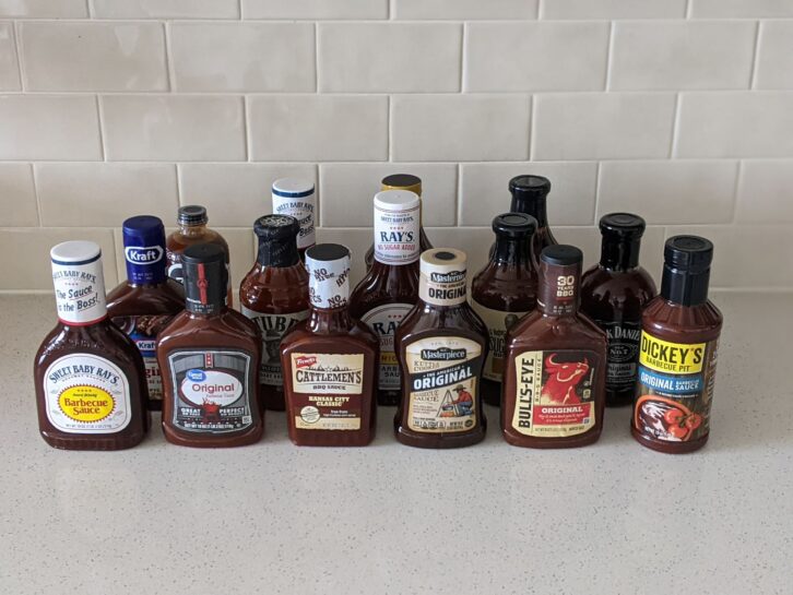 15 bottles of BBQ for a taste test on a beige countertop, beige kitchen wall tile in the background